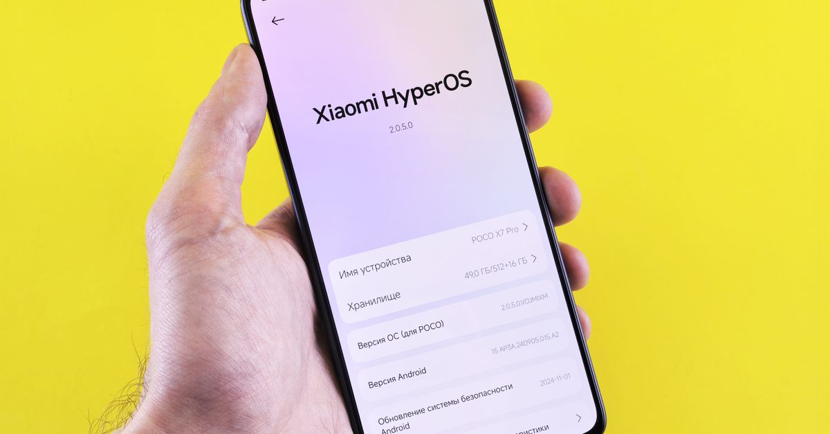 Close-up of a smartphone displaying Xiaomi HyperOS interface, held by a hand against a bright yellow background.